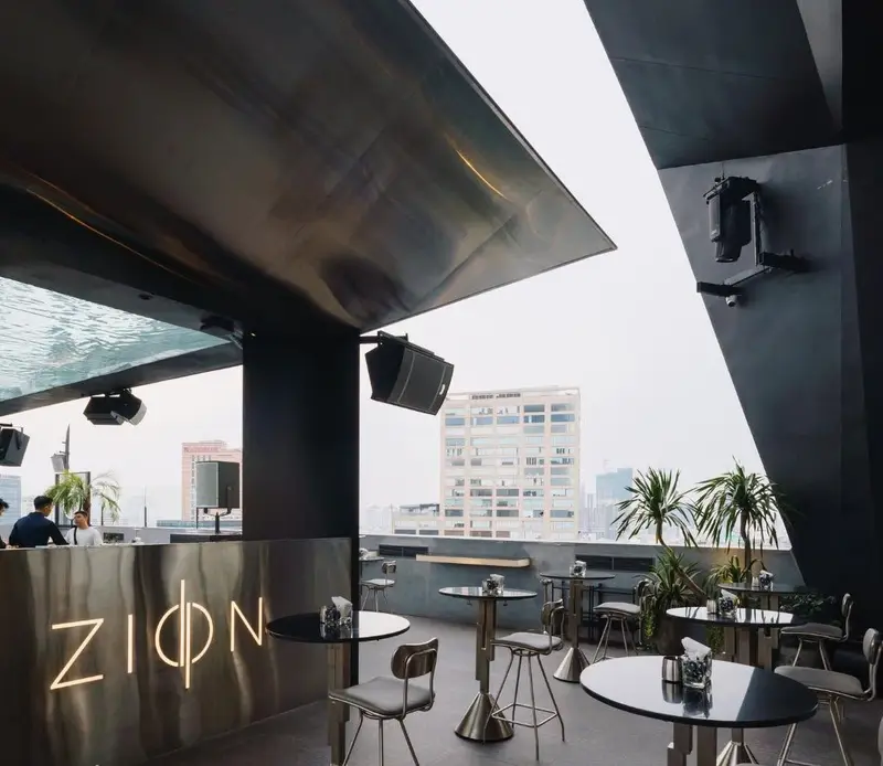 Sân ngoài trời tầng 14 của Zion với quầy kim loại chữ ZION phát sáng, mái kim loại cong và các toà nhà phía xa